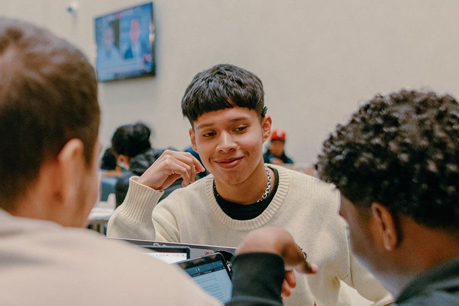 student of color grinning and back of 2 other students facing him