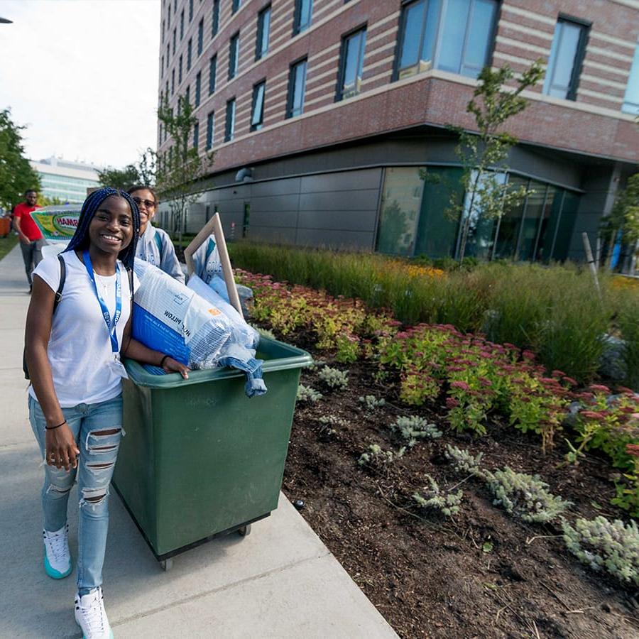 A student pulls a bin of things towards dorm on move in day.